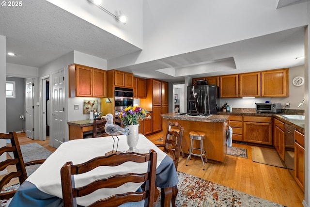 16165 NW Blueridge Dr, Beaverton, OR 97006 - kitchen with appliances with stainless steel finishes, light wood-type flooring, a kitchen island, brown cabinets, and dark countertops