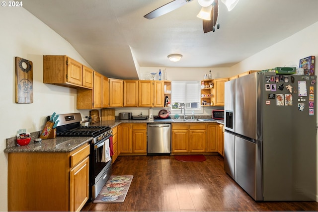 kitchen featuring ceiling fan, dark stone countertops, sink, dark wood-type flooring, and appliances with stainless steel finishes