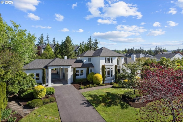 view of front of house featuring stucco siding, asphalt driveway, an attached carport, a front lawn, and a residential view