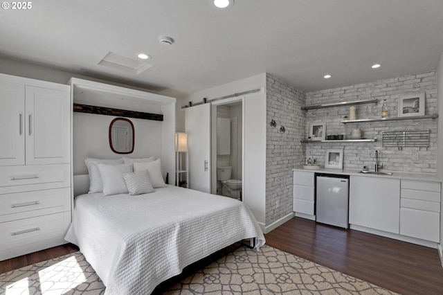 bedroom with wood finished floors, bar with sink, a barn door, recessed lighting, and fridge