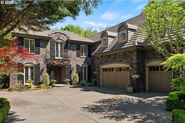 french country inspired facade featuring stone siding, concrete driveway, and an attached garage