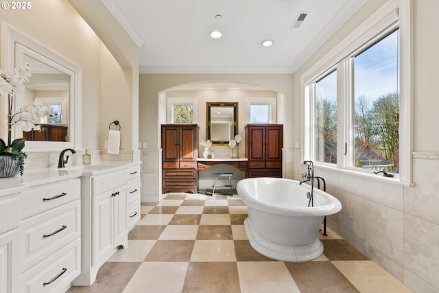 full bath with tile walls, a freestanding bath, healthy amount of natural light, crown molding, and a wainscoted wall