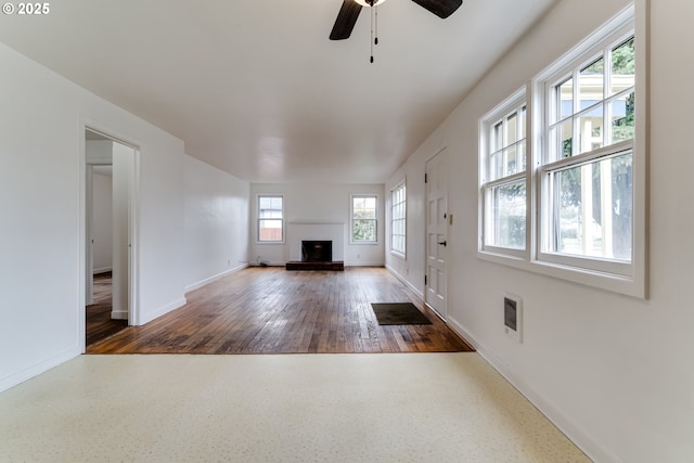 unfurnished living room with baseboards, a fireplace with raised hearth, and a ceiling fan