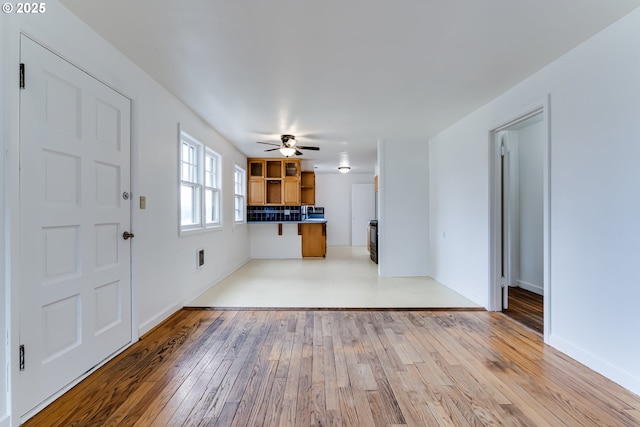 unfurnished living room featuring a ceiling fan, light wood-type flooring, and baseboards