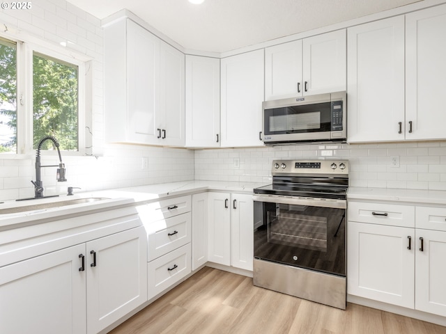 13928 SE Rhone St, Portland, OR 97236 - kitchen featuring appliances with stainless steel finishes, a sink, tasteful backsplash, white cabinets, and light wood-style flooring