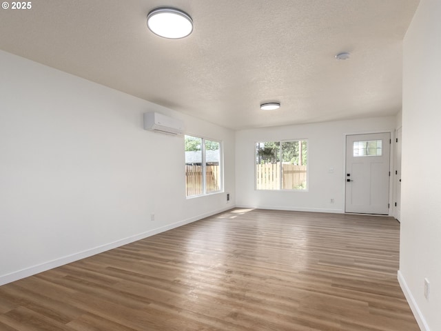 13928 SE Rhone St, Portland, OR 97236 - unfurnished living room featuring a wall unit AC, wood finished floors, healthy amount of natural light, baseboards, and a textured ceiling