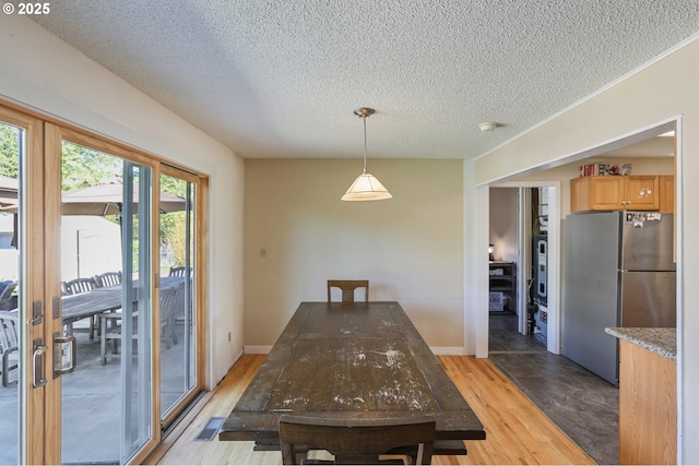 dining room featuring a textured ceiling, light wood finished floors, and baseboards