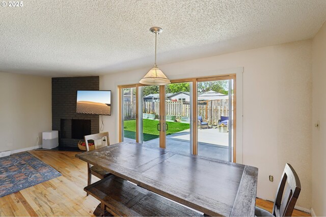 dining room with wood finished floors, a textured ceiling, and a brick fireplace
