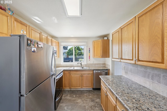kitchen with appliances with stainless steel finishes, a sink, decorative backsplash, and light stone countertops