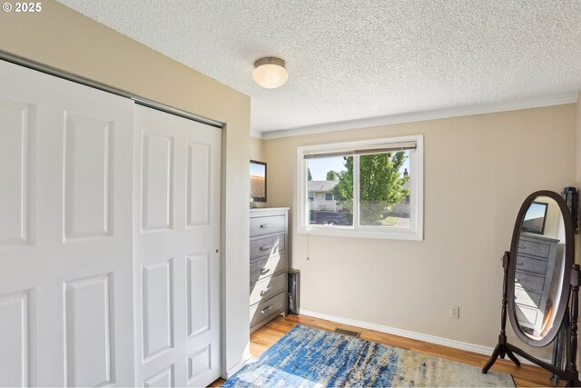 bedroom featuring a textured ceiling, light wood-type flooring, a closet, and baseboards