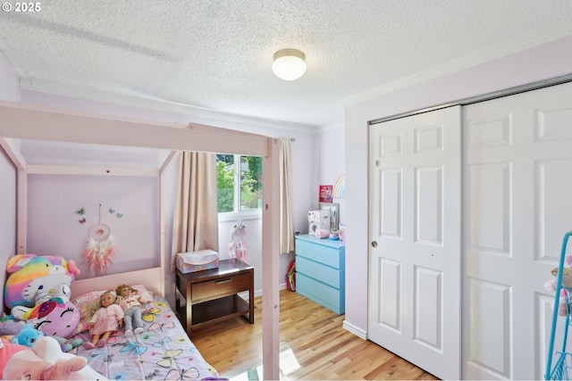 bedroom with ornamental molding, a textured ceiling, light wood-style floors, and a closet