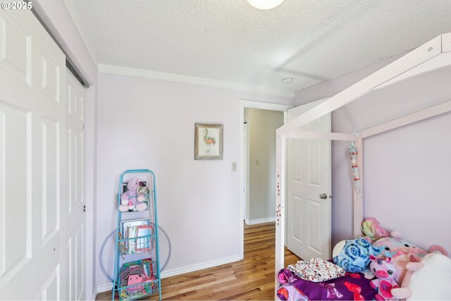 bedroom featuring light wood-style floors, a textured ceiling, a closet, crown molding, and baseboards
