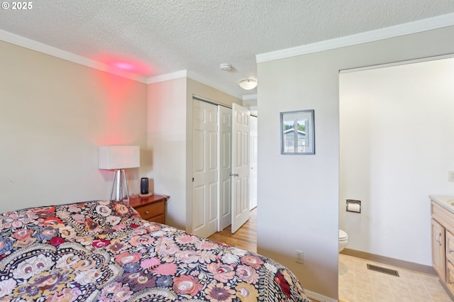 bedroom with crown molding, a closet, a textured ceiling, light flooring, and ensuite bathroom