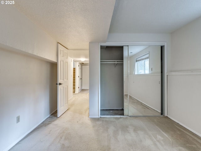 unfurnished bedroom featuring light carpet, a closet, and a textured ceiling