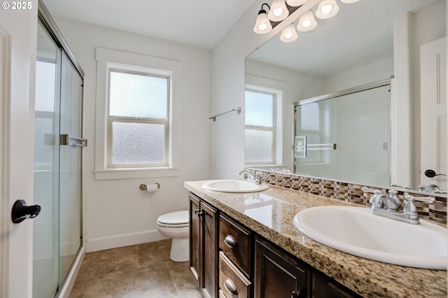 bathroom featuring a stall shower, double vanity, a sink, and baseboards
