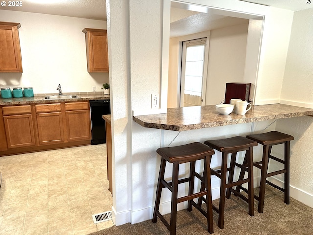 kitchen with dishwasher, a sink, brown cabinets, and a breakfast bar area