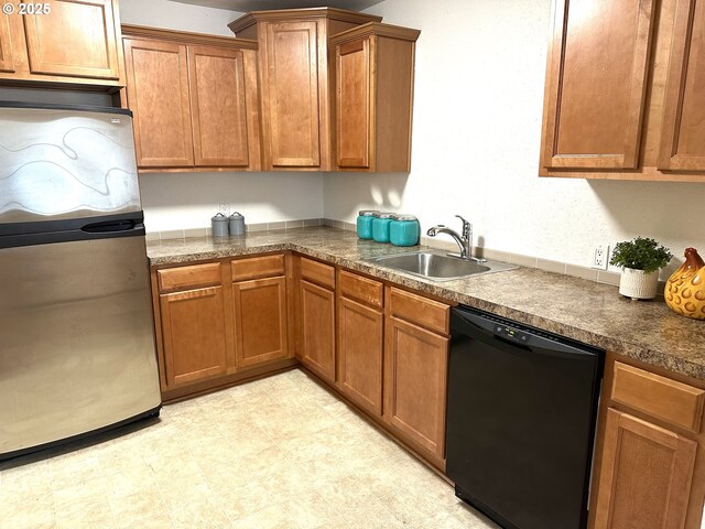 kitchen with dishwasher, brown cabinets, a sink, and freestanding refrigerator
