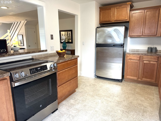kitchen featuring light floors, stainless steel appliances, brown cabinets, and dark stone counters