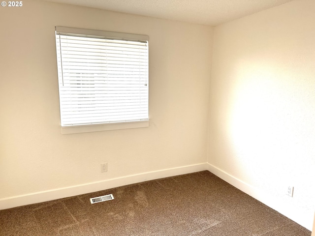 empty room with baseboards, visible vents, and dark carpet