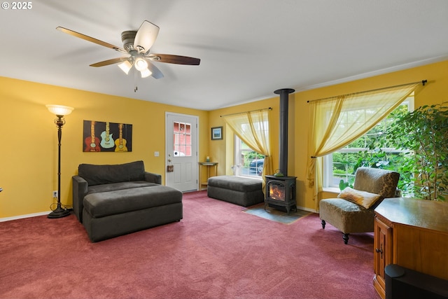 living area featuring a wood stove, a ceiling fan, carpet flooring, and baseboards