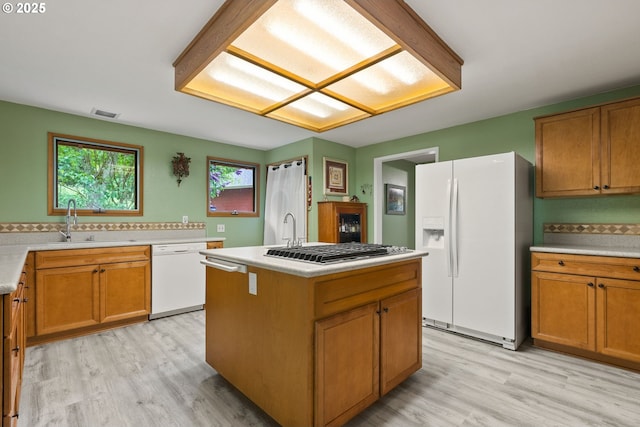 kitchen featuring white appliances, a sink, light wood-style flooring, and a kitchen island with sink