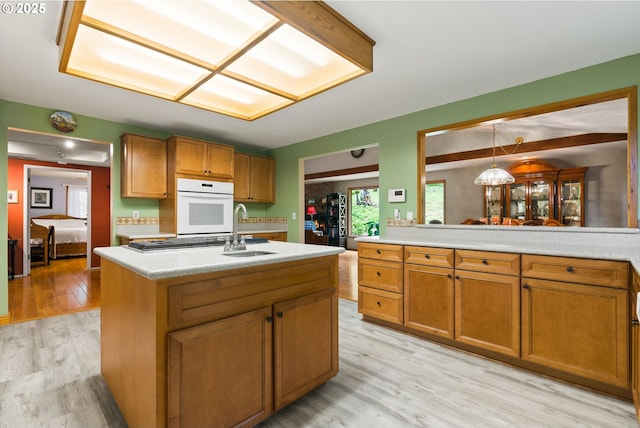 kitchen with a sink, white oven, light wood-style floors, and brown cabinets