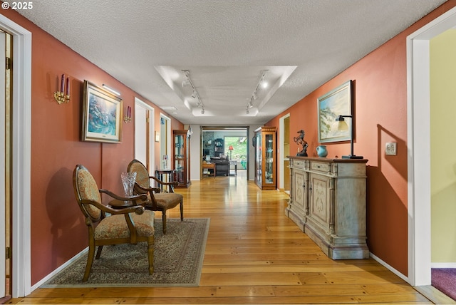 hallway featuring light wood-style floors, a textured ceiling, rail lighting, and baseboards