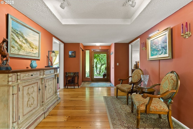 entryway with a textured ceiling, light wood finished floors, a raised ceiling, and baseboards