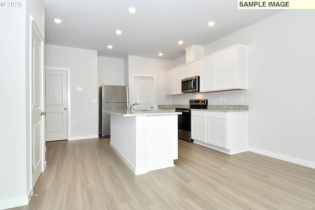 kitchen with light hardwood / wood-style flooring, an island with sink, stainless steel appliances, light stone countertops, and white cabinets