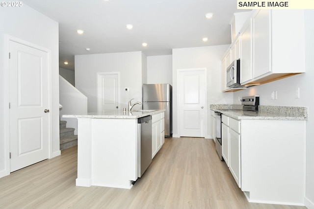 kitchen featuring light stone counters, stainless steel appliances, a kitchen island with sink, and white cabinets