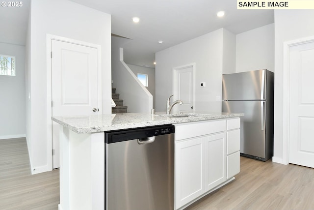 kitchen featuring appliances with stainless steel finishes, white cabinetry, a kitchen island with sink, light stone countertops, and light wood-type flooring