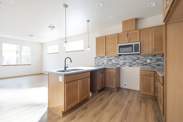 kitchen with tasteful backsplash, sink, pendant lighting, and light hardwood / wood-style flooring