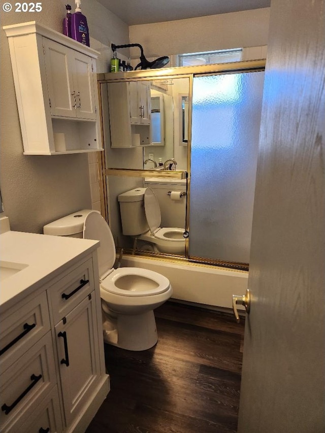 full bathroom with combined bath / shower with glass door, vanity, hardwood / wood-style flooring, and toilet