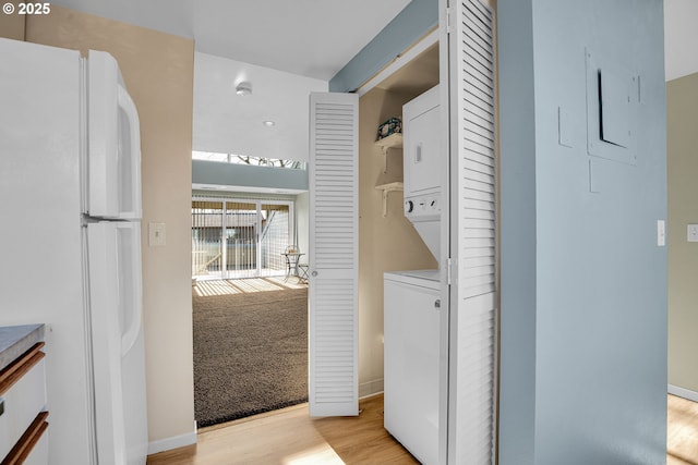 washroom featuring stacked washer / drying machine, baseboards, laundry area, and light wood finished floors