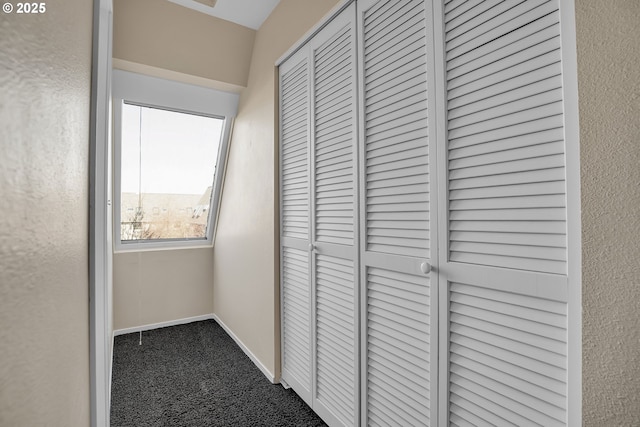 hallway featuring baseboards and dark carpet