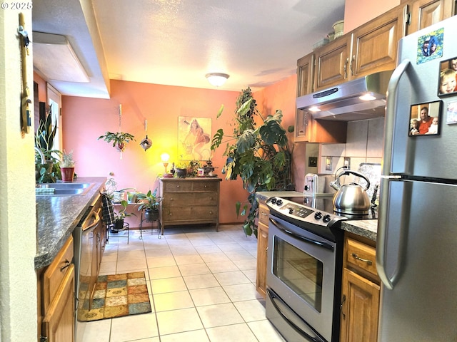 kitchen featuring a textured ceiling, stainless steel appliances, sink, dark stone countertops, and light tile patterned flooring