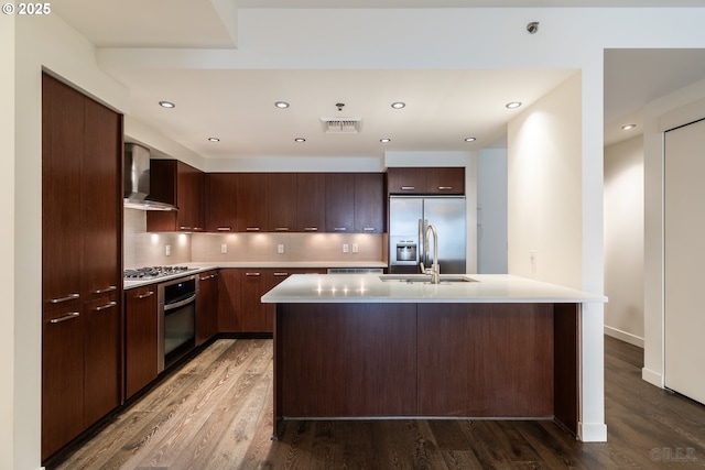 kitchen with stainless steel appliances, a kitchen island with sink, sink, and wall chimney exhaust hood