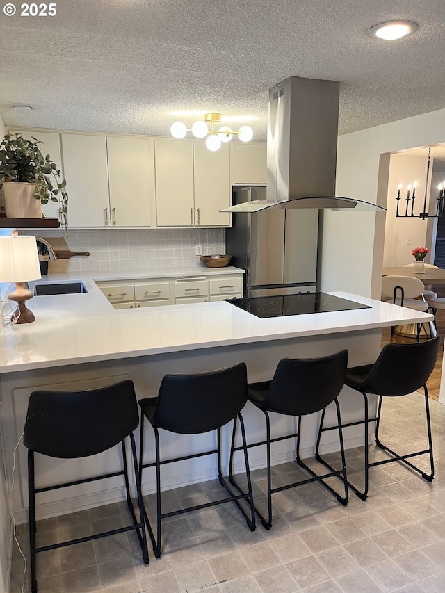 kitchen with a sink, a textured ceiling, black electric stovetop, island exhaust hood, and a breakfast bar area