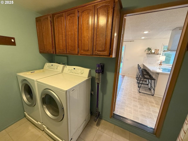laundry area with light tile patterned floors, baseboards, washer and dryer, a textured ceiling, and cabinet space