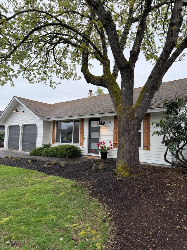 ranch-style house featuring roof with shingles, a front lawn, a garage, and concrete driveway
