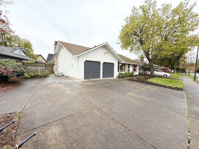view of side of home featuring central AC, an attached garage, a chimney, fence, and concrete driveway