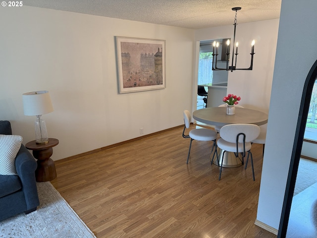 dining space with a notable chandelier, a textured ceiling, baseboards, and wood finished floors