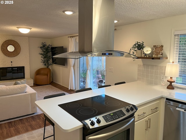kitchen featuring island range hood, a peninsula, a textured ceiling, and appliances with stainless steel finishes