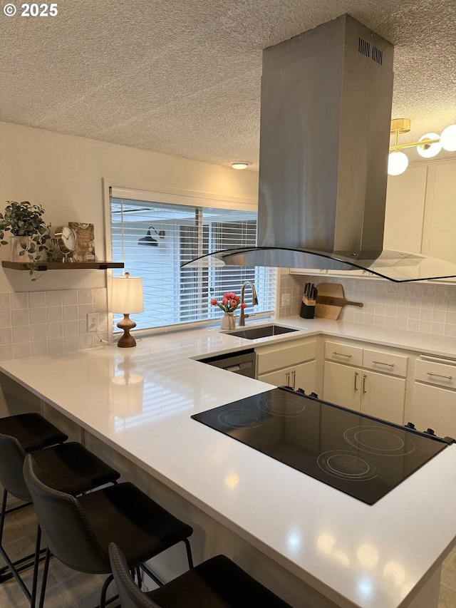 kitchen featuring a textured ceiling, white cabinets, decorative backsplash, island range hood, and a sink