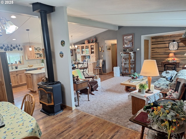 living room with a notable chandelier, lofted ceiling with beams, a wood stove, light wood-style floors, and recessed lighting