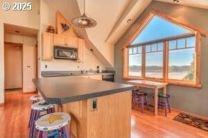 52995 Riverview Dr, La Pine, OR 97739 - kitchen featuring light wood-style flooring, a kitchen island, dark countertops, a breakfast bar, and pendant lighting