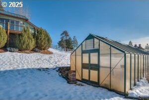 snow covered structure featuring a greenhouse and an outdoor structure