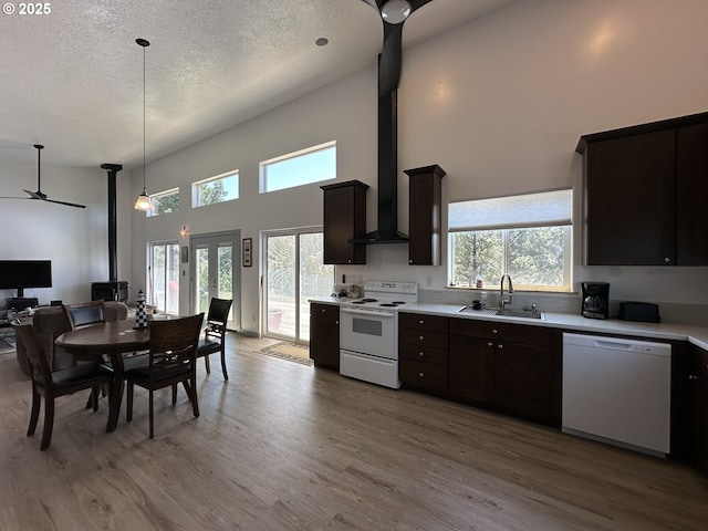 kitchen featuring light wood-type flooring, a sink, light countertops, a high ceiling, and white appliances
