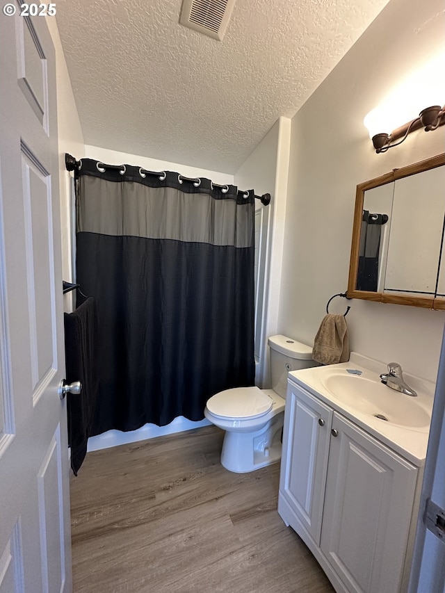 bathroom with vanity, toilet, a textured ceiling, wood finished floors, and visible vents