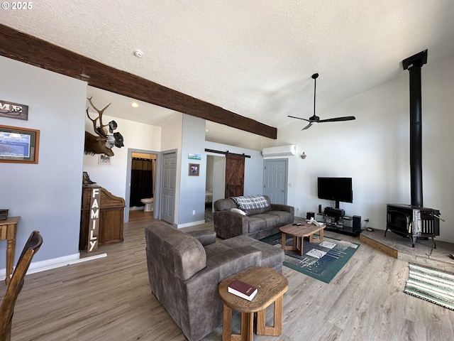 living area featuring light wood-type flooring, a barn door, a textured ceiling, a wall unit AC, and a ceiling fan